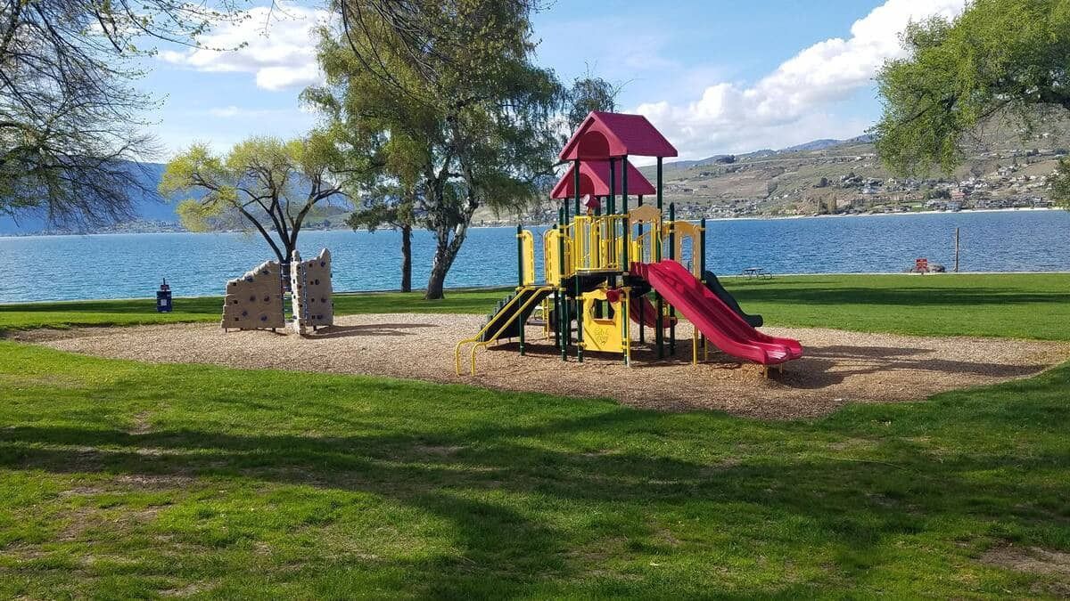 Une aire de jeux avec un toboggan et des structures d’escalade, située près d’une étendue d’eau.