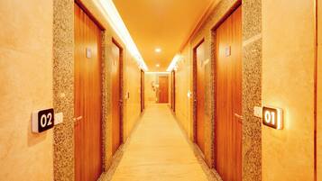 Pasillo de hotel con puertas numeradas, piso alfombrado e iluminación en el techo.