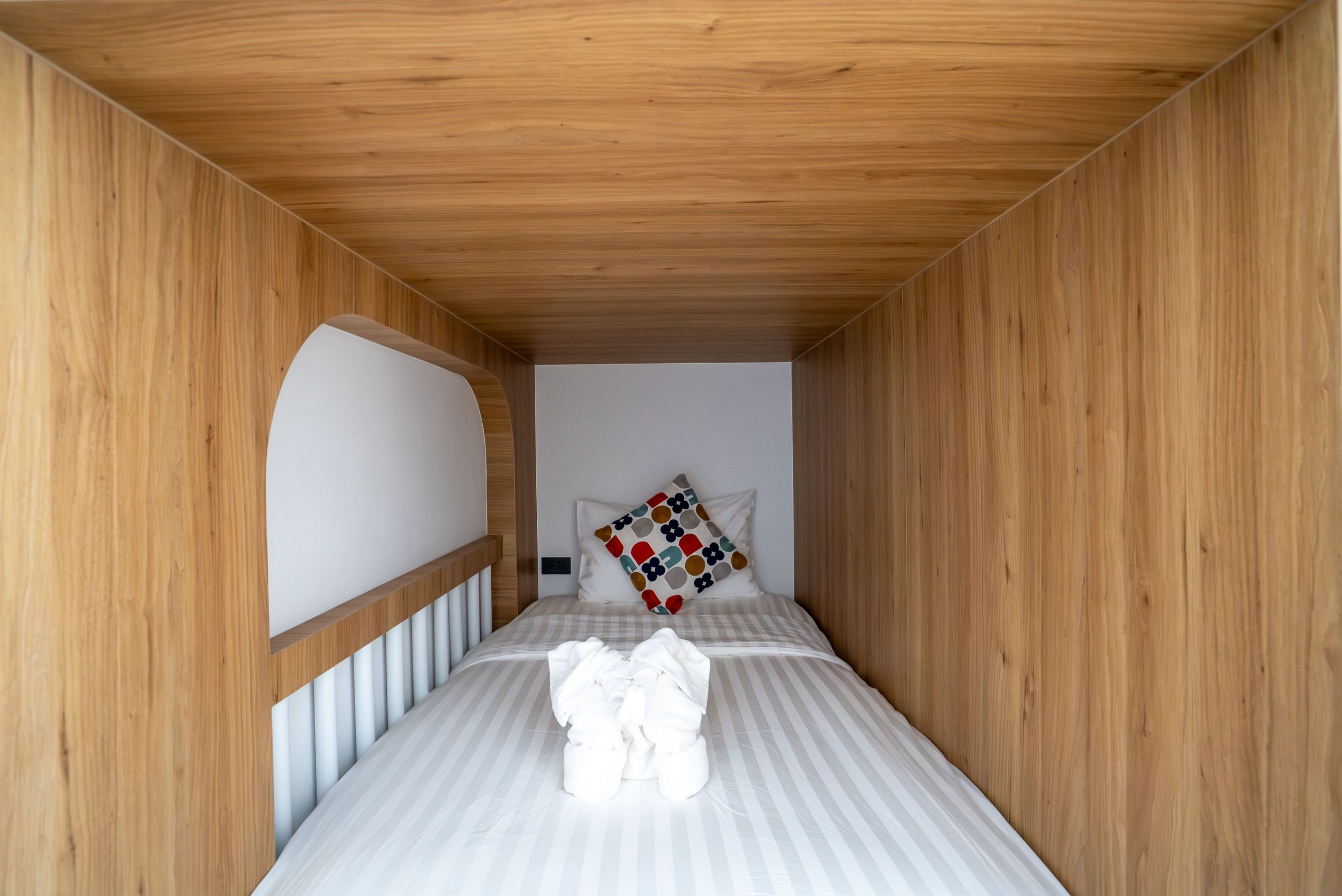 A small, narrow room with a single bed, a wooden ceiling, and a white wall.