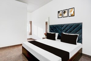 Une chambre à coucher moderne avec un grand lit, une tête de lit sombre et trois œuvres d’art encadrées accrochées au mur.