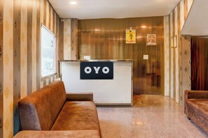 Un espace d’accueil avec un comptoir de réception portant l’inscription « OYO », un canapé en cuir marron et un mur orné de motifs.