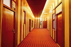 Un couloir d’hôtel avec des portes en bois et un sol recouvert de moquette.