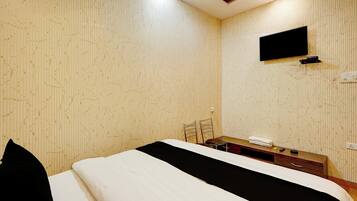 Habitación de hotel con cama, televisor de pantalla plana en la pared, mesita de noche con lámpara y toma de corriente.