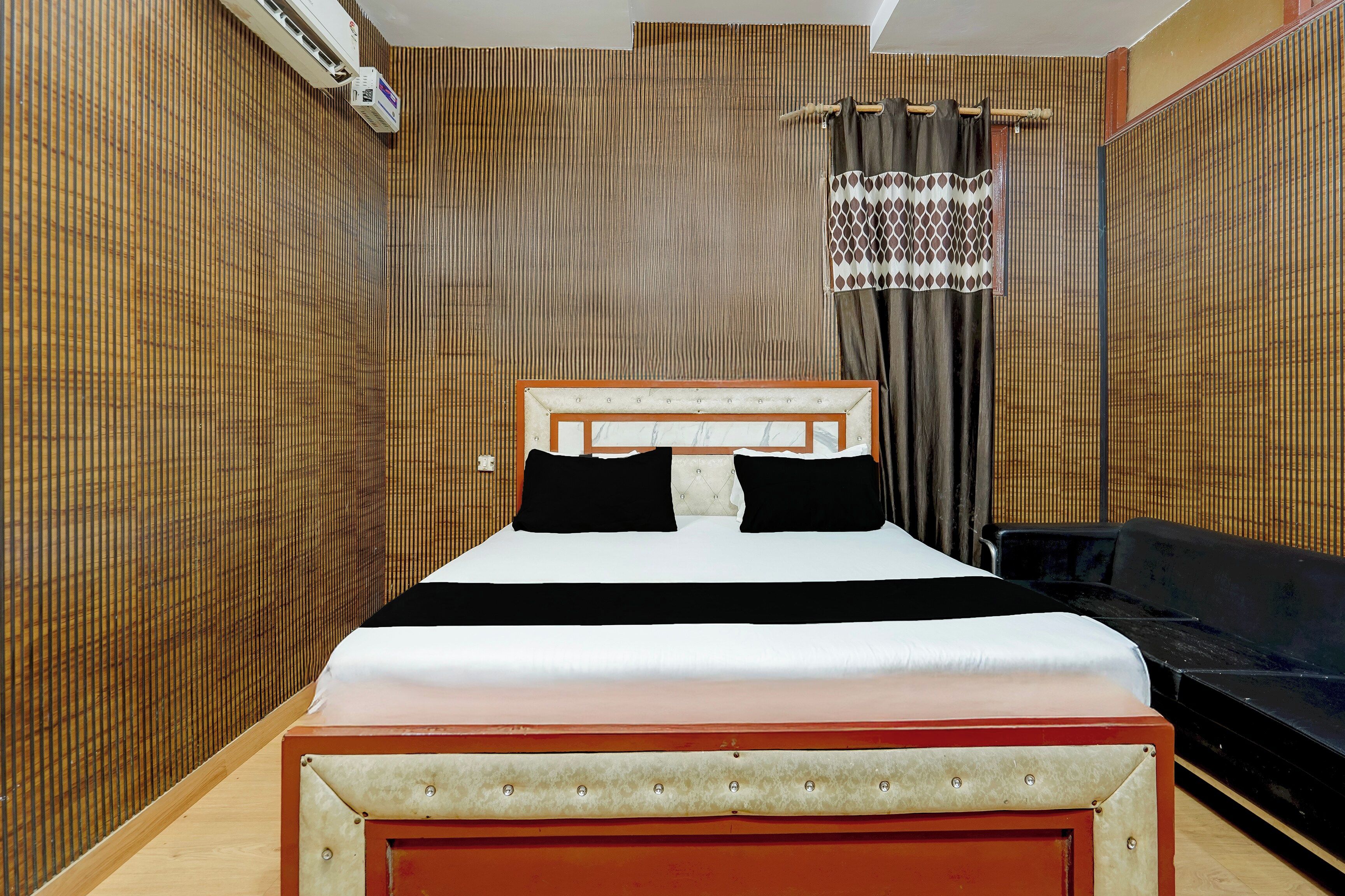 A hotel room with a bed, a television, and a wall-mounted air conditioning unit.
