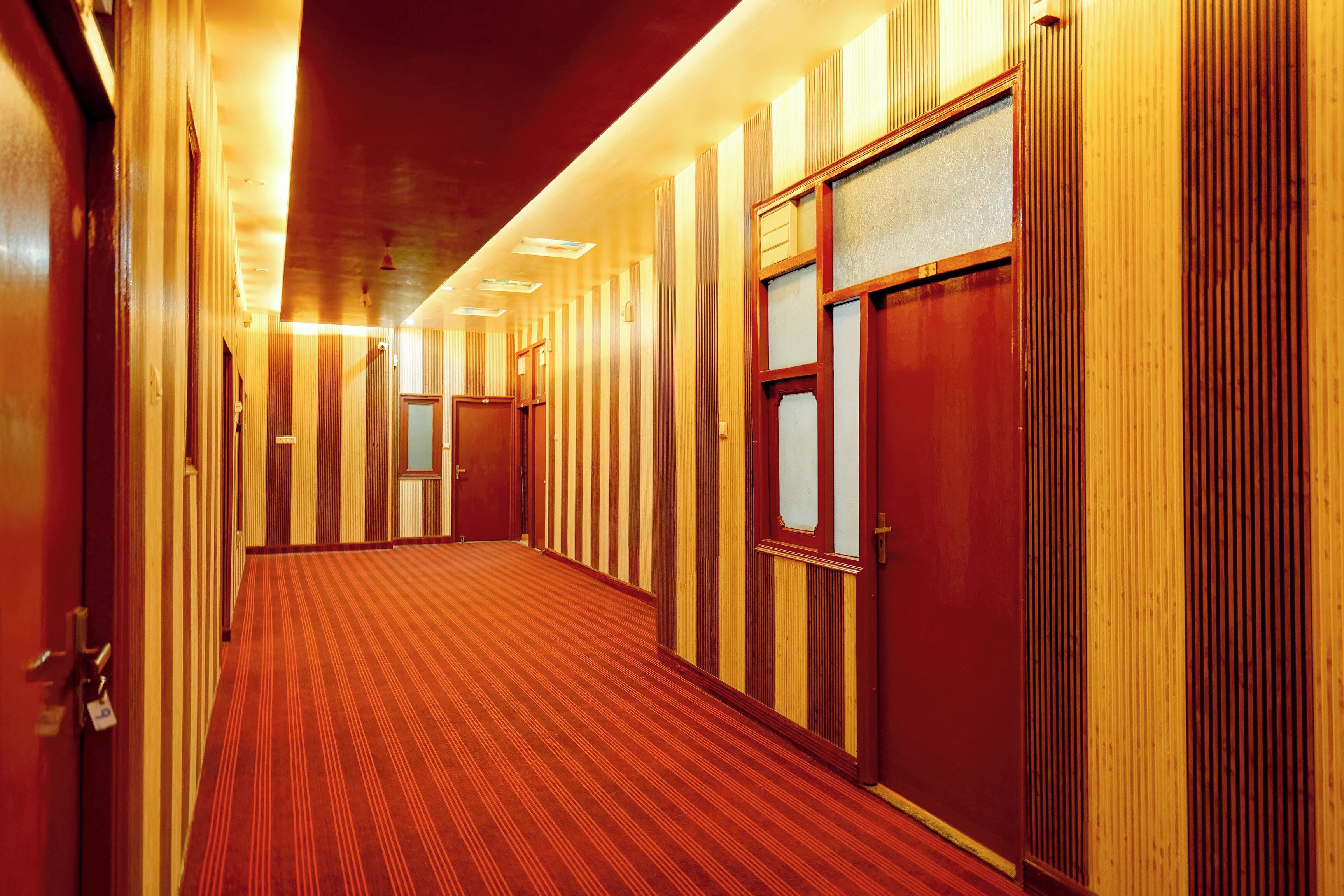 Un pasillo de hotel con paneles de madera, alfombra roja y puertas con vidrios esmerilados.