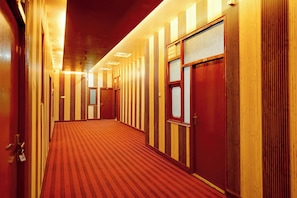 A hotel corridor with wooden paneling, a red carpet, and doors with frosted glass panels.