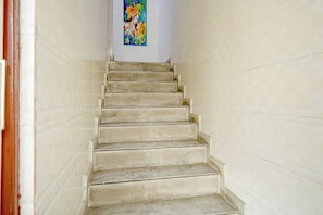 Un escalier menant à une pièce dont le mur est orné d’un tableau religieux aux couleurs vives.