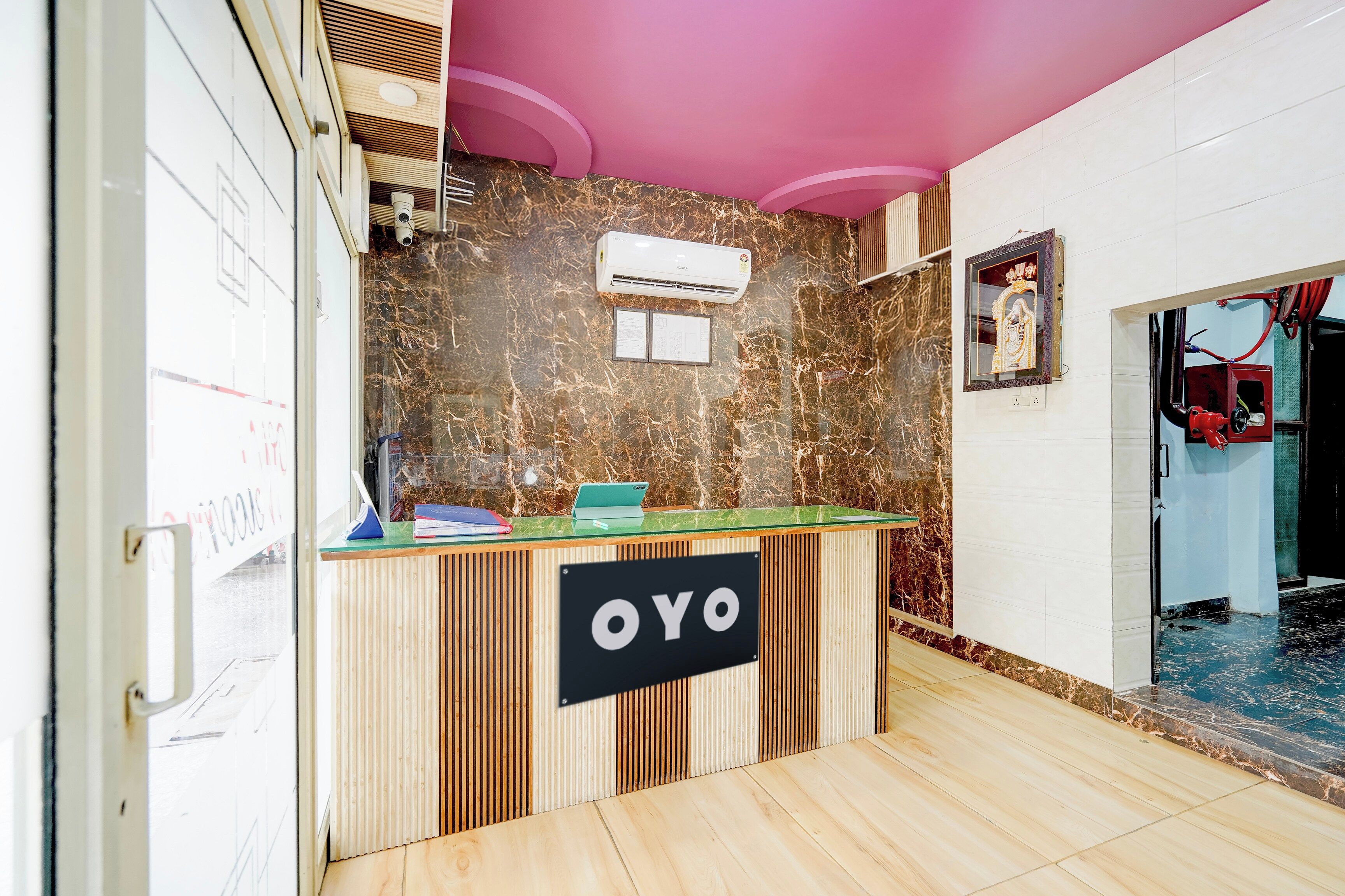 A reception desk with a sign reading 'OYO,' a marble wall, and a ceiling with a pink accent.