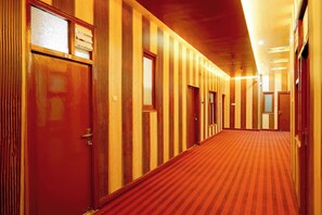A hotel corridor with wooden paneling, a red carpet, and multiple doors.