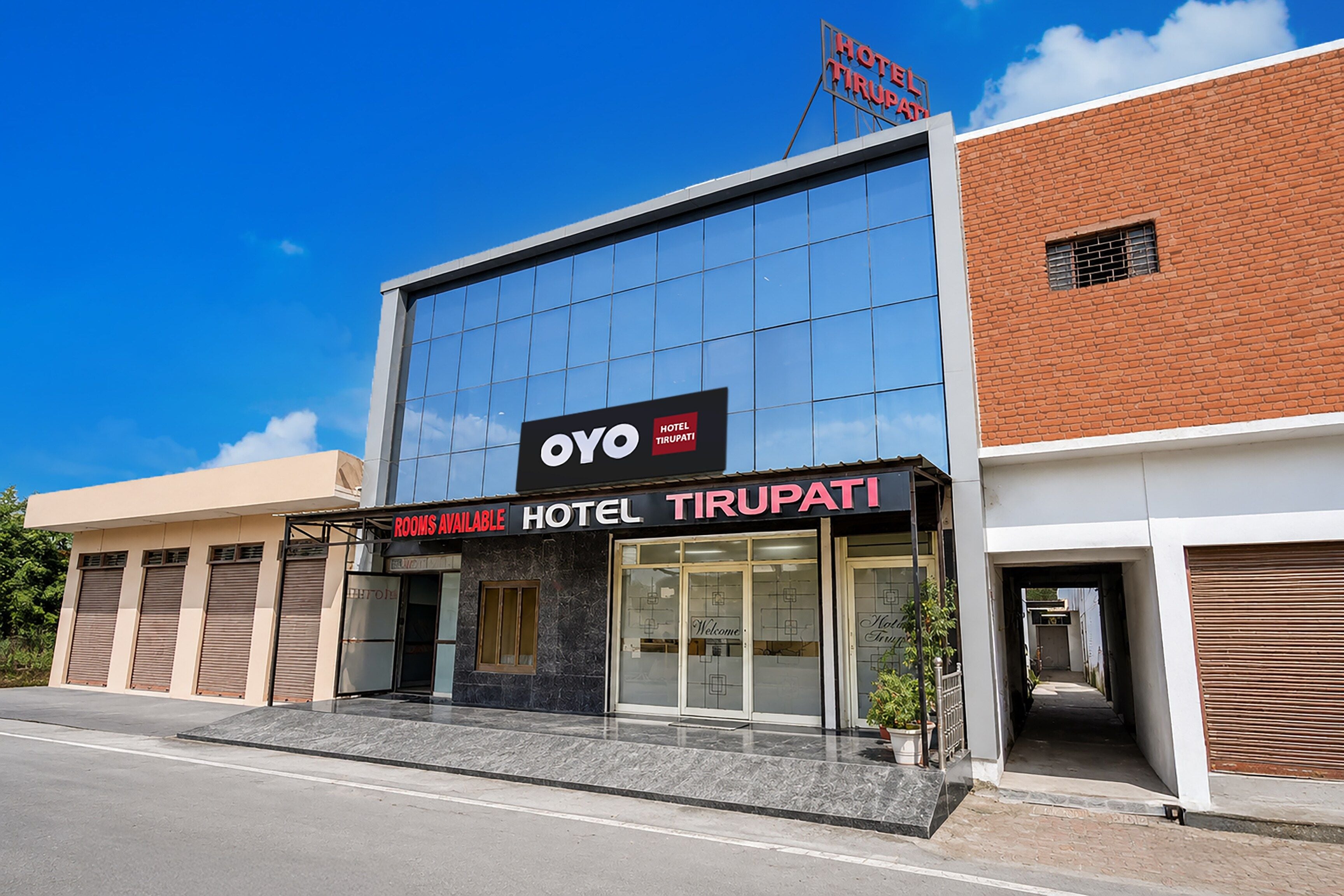 A modern hotel building with a sign indicating 'Rooms Available' and 'Hotel Tirupati'.