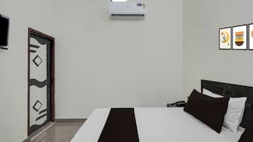 A hotel room with a bed, a desk with a phone, an air conditioning unit, a door with a geometric design, and framed artwork on the wall.