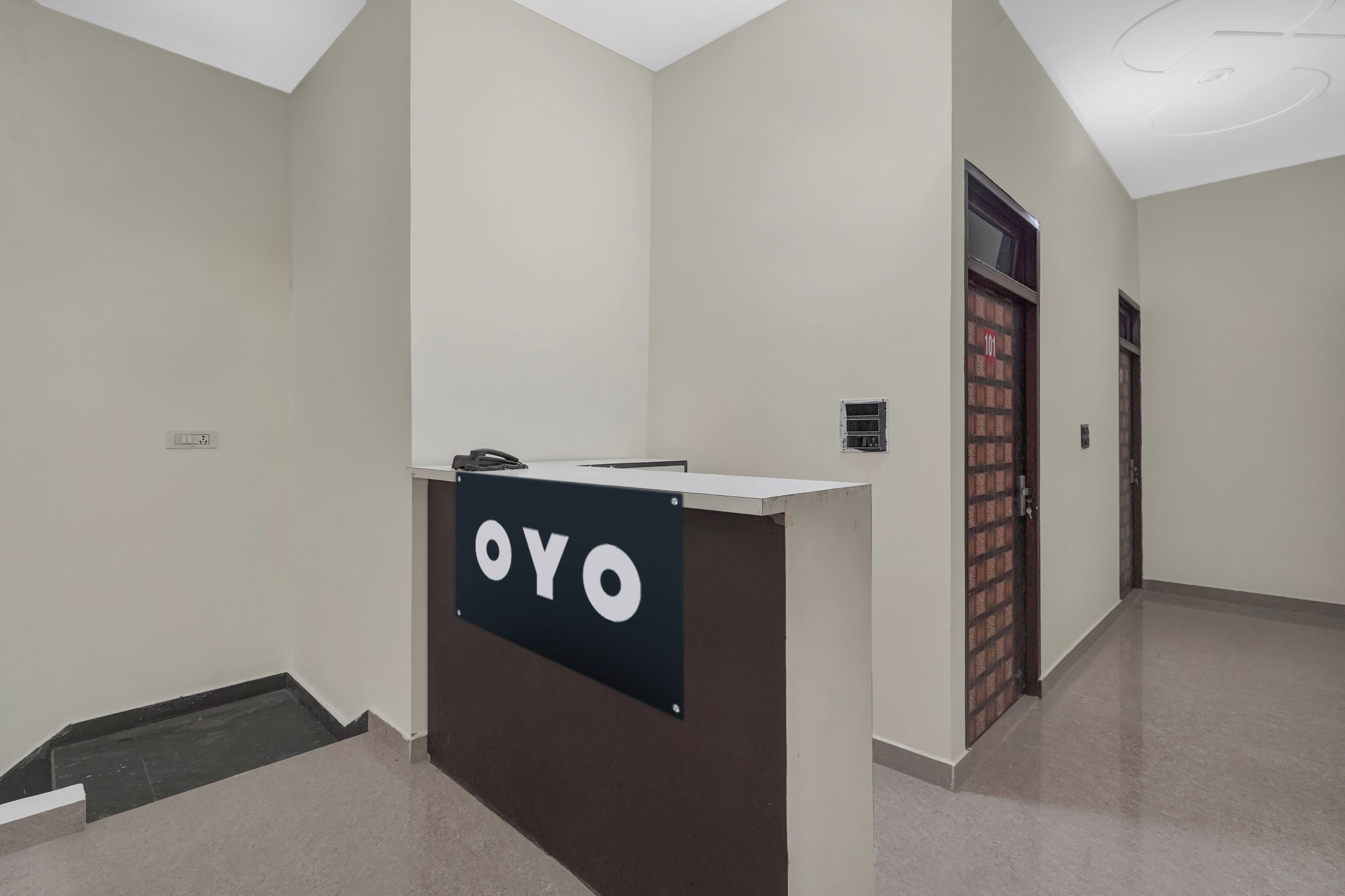 A reception desk with a sign reading 'OYO' in a hallway with white walls and a tiled floor.