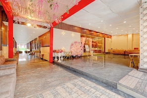 Vestíbulo de hotel con piso de mármol, pilares rojos y mostrador de recepción.