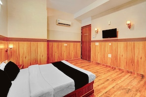 Une chambre d’hôtel avec un plancher en bois, un lit avec une literie blanche, un téléviseur fixé au mur et un appareil de climatisation.