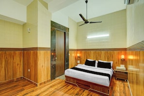 A hotel room with a bed, wooden paneling, a ceiling fan, and a nightstand with a lamp. - HOTEL O SAFFRON (Meerut)