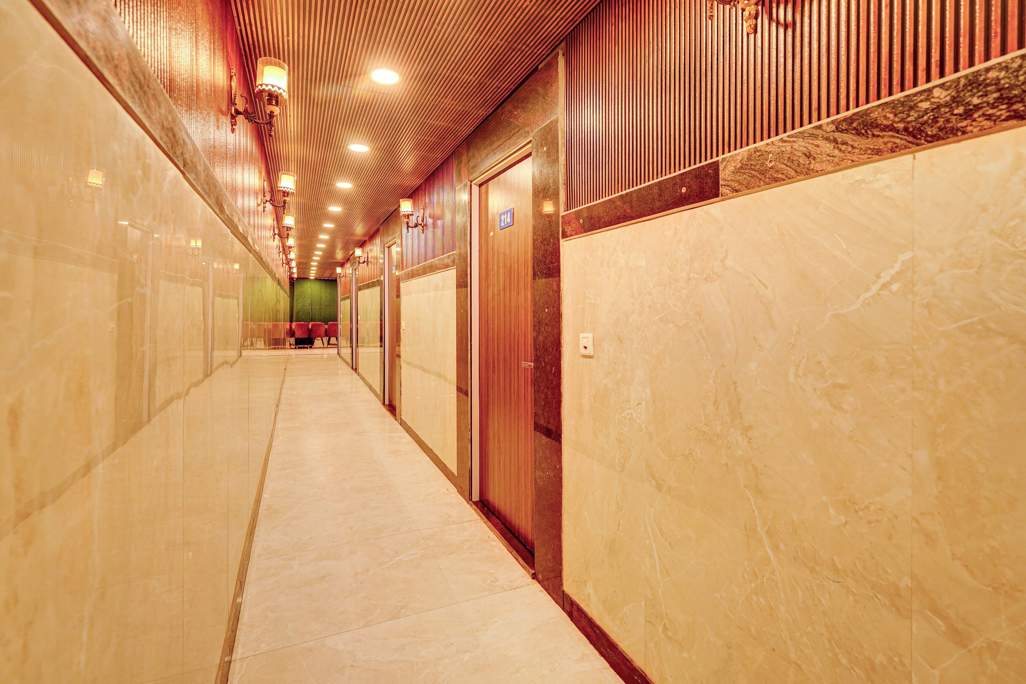 Un pasillo de hotel con piso de mármol, paneles de madera en el techo y una pared verde al final.