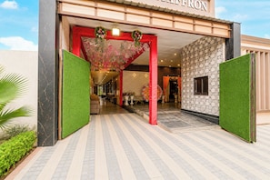 Entrada de hotel con un arco rojo, césped artificial verde y paredes con diseño.