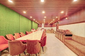 A conference room with a long table, red chairs, a green wall, a wooden ceiling, and a reception desk with a counter. - HOTEL O SAFFRON (Meerut)