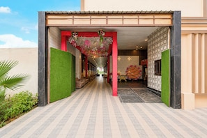 L’entrée d’un hôtel, avec un passage couvert, des murs recouverts de verdure et un sol carrelé.
