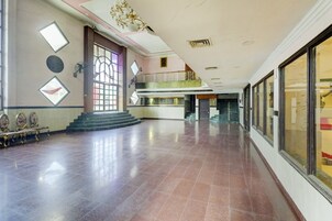 A spacious lobby with a marble floor, a staircase leading to an upper level, and a large window with decorative elements.