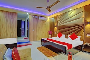 A hotel room with a bed, a sofa, a glass coffee table, a ceiling fan, and a wall-mounted air conditioner. - Hotel O by OYO Island (Meerut)