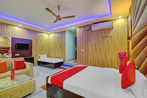 A hotel room with a bed, a sofa, a TV, and a ceiling fan. - Hotel O by OYO Island (Meerut)