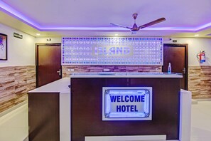 A reception desk with a 'Welcome Hotel' sign, a ceiling fan, and a wall with a 'ISLAND' sign.