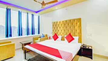 Quarto de hotel com cama grande, ventoinha no teto, mesa de cabeceira e janela com cortinas.