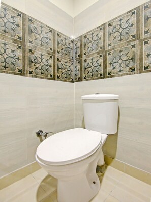Un baño con inodoro blanco, paredes con azulejos y un diseño en esquina.
