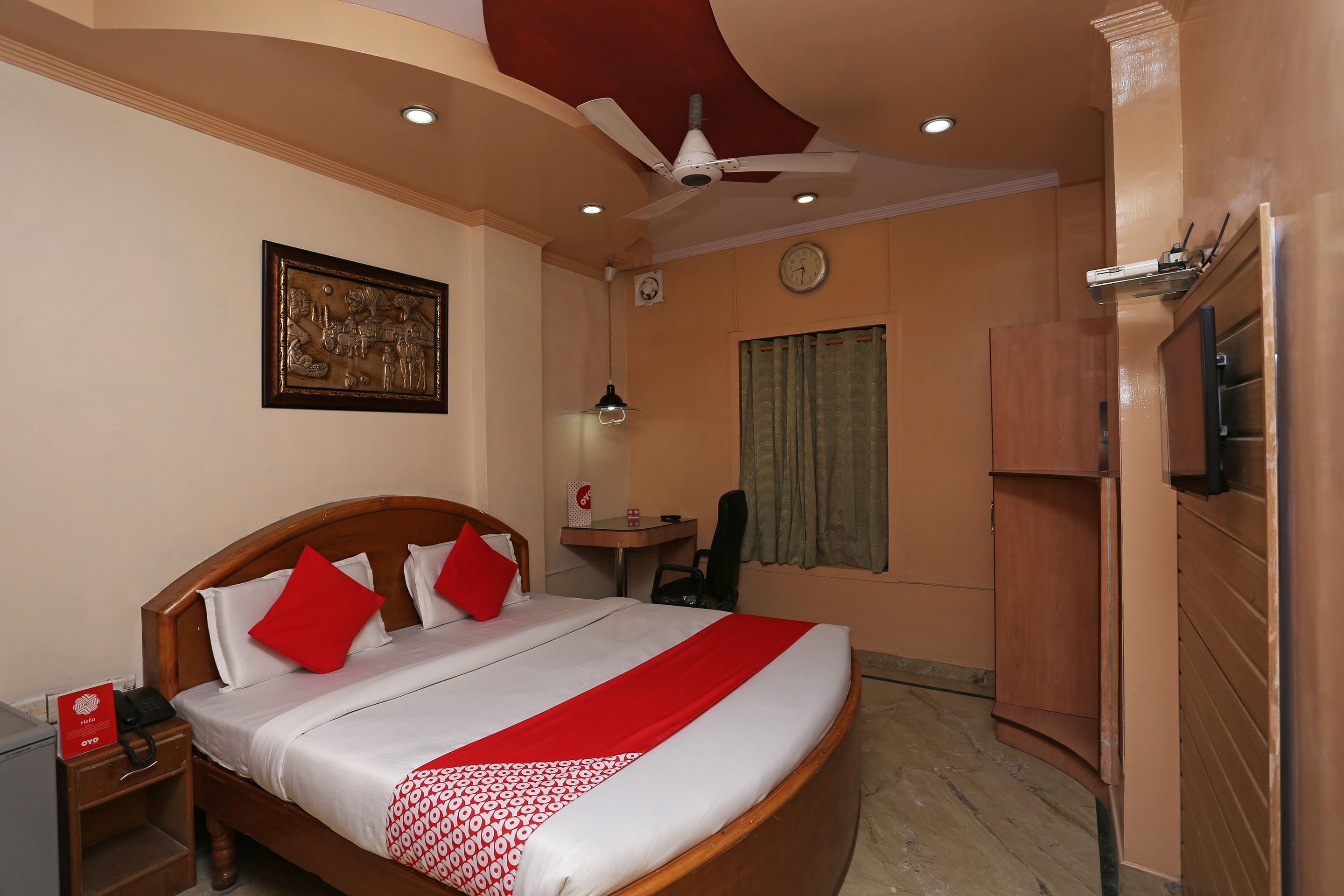 A hotel room with a large bed, a desk, a chair, a television, and a ceiling fan.