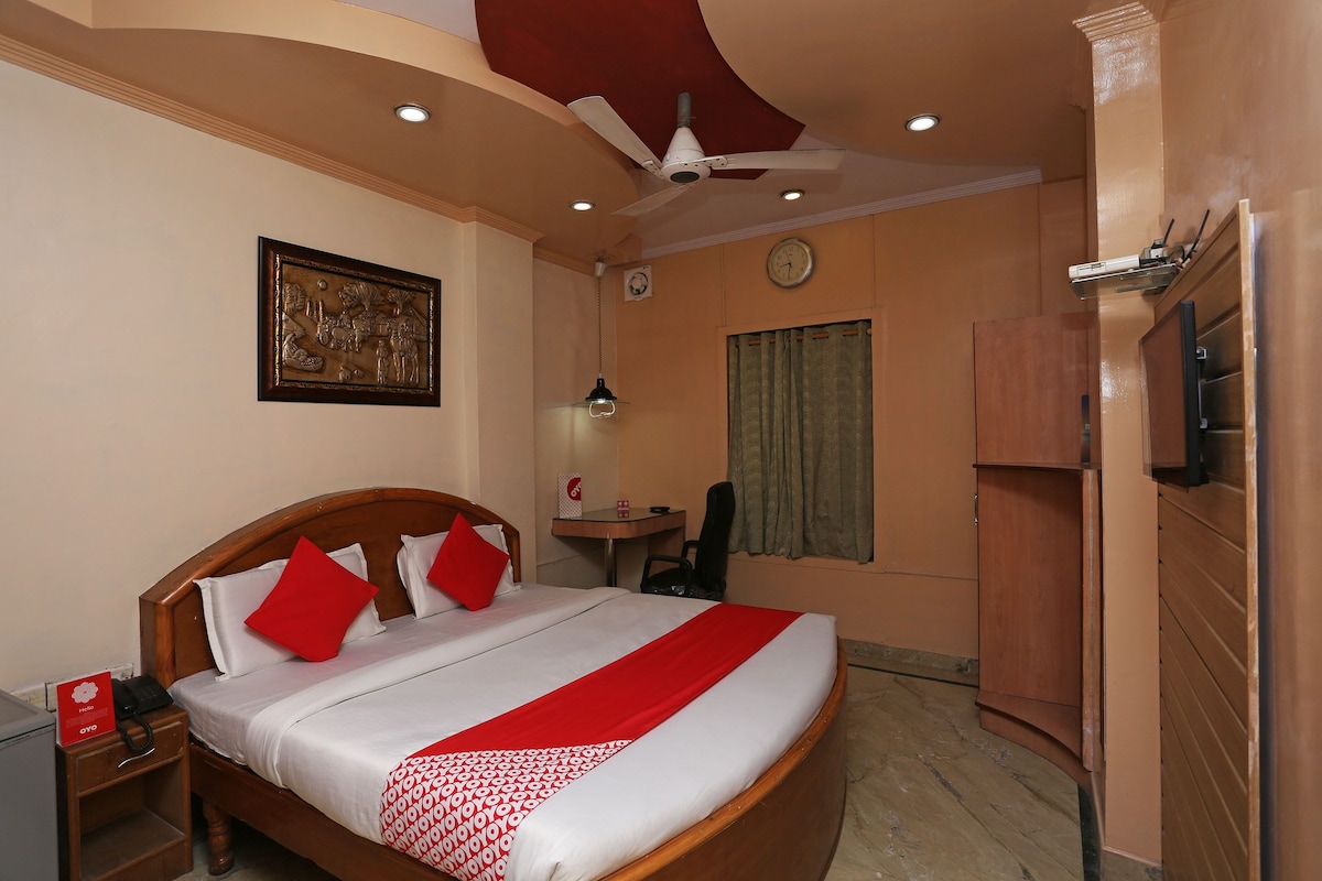 A hotel room with a large bed, a desk, a chair, a television, and a ceiling fan.