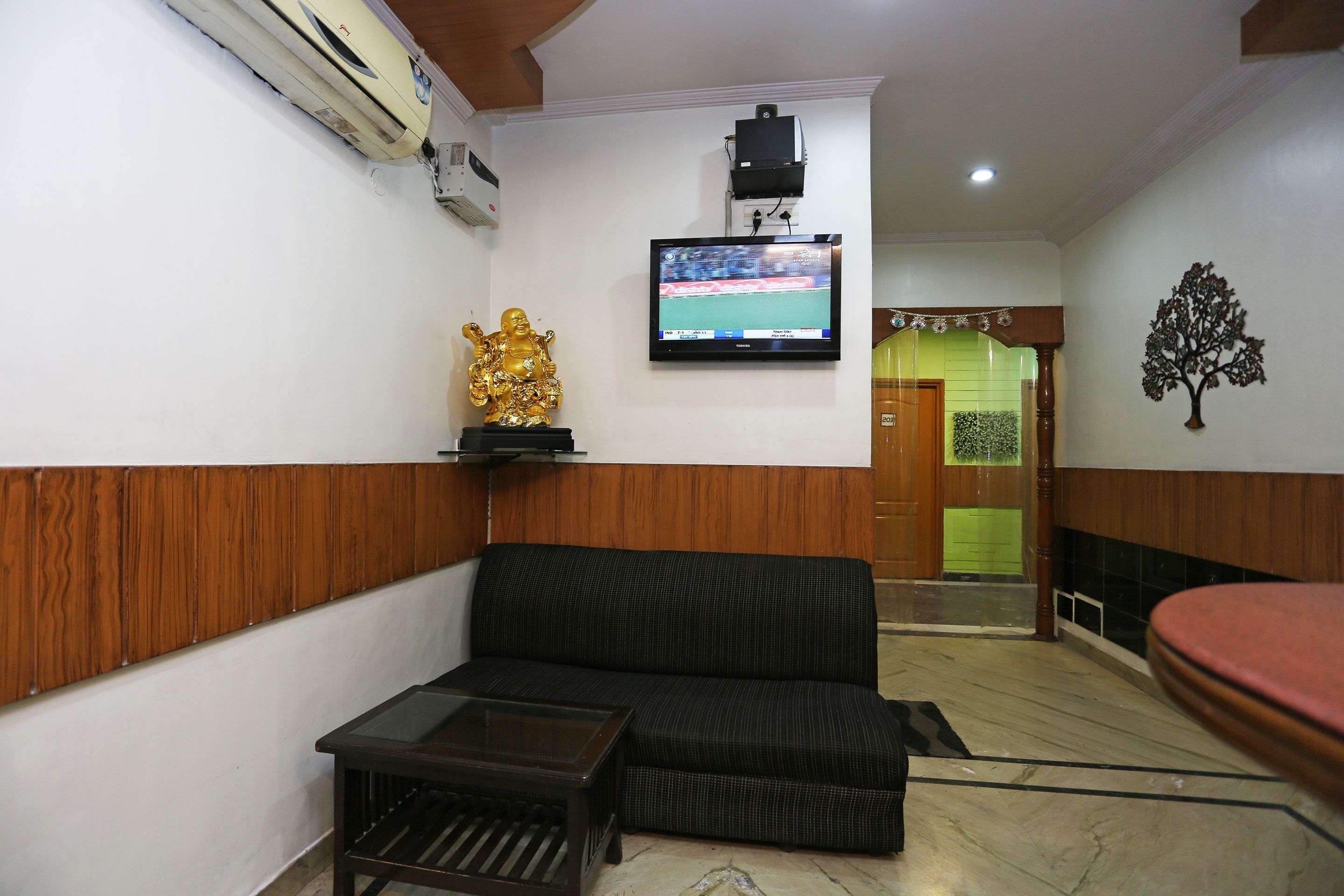 Una sala de estar con un sofá, una mesita, un televisor montado en la pared y una estatua dorada decorativa.