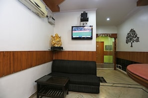 A living room with a sofa, a small table, a television mounted on the wall, and a decorative golden statue.
