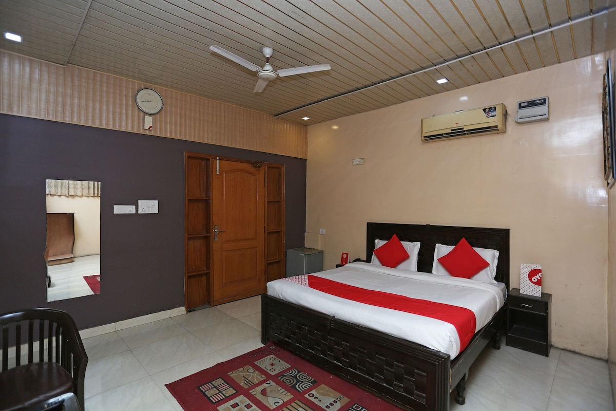 A hotel room with a bed, a ceiling fan, an air conditioning unit, a clock, and a mirror.