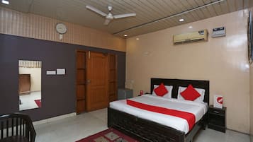 A hotel room with a bed, a ceiling fan, an air conditioning unit, a clock, and a mirror.