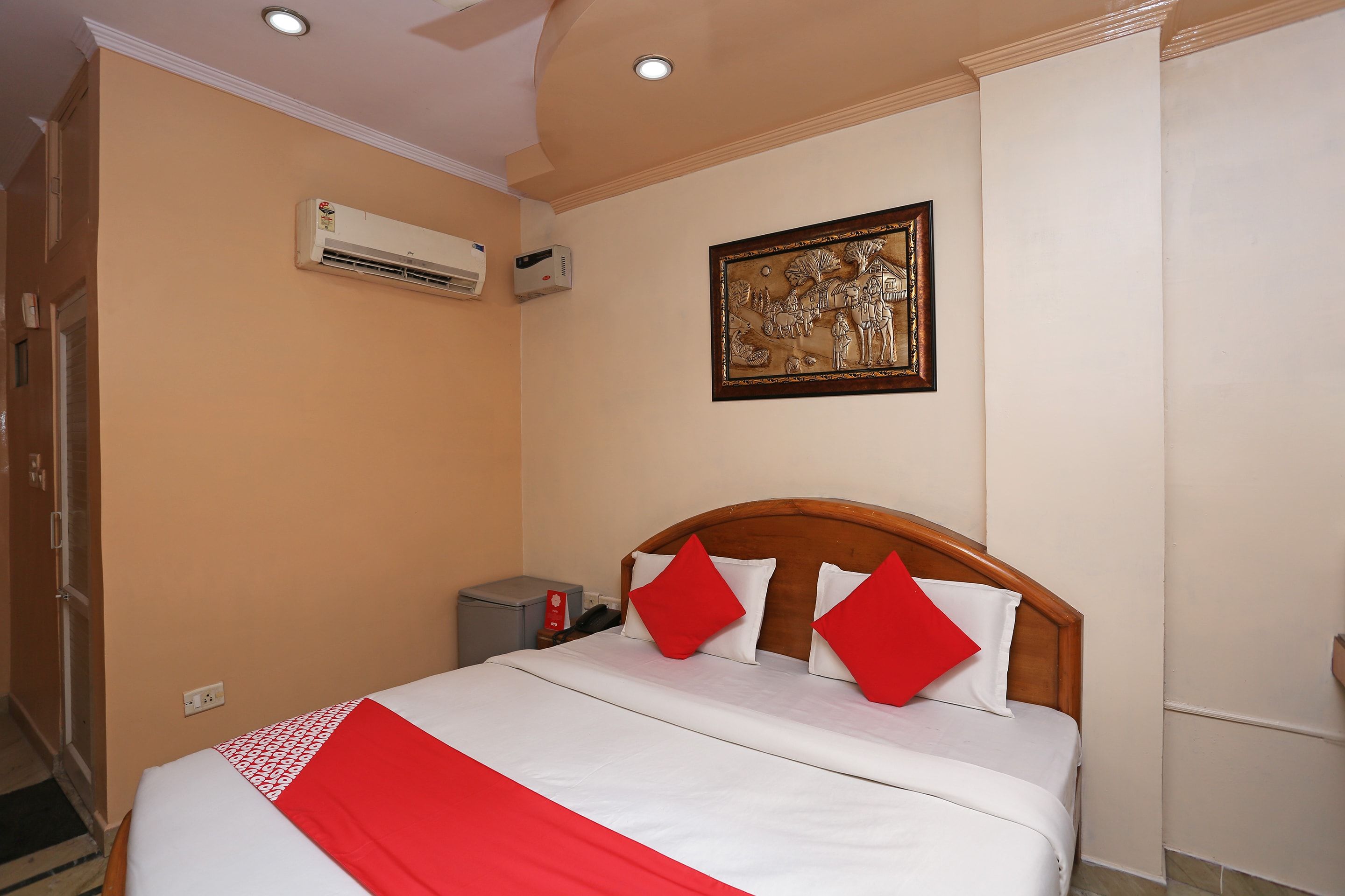 Habitación de hotel con cama, mesita de noche, unidad de aire acondicionado, un cuadro en la pared y una puerta.