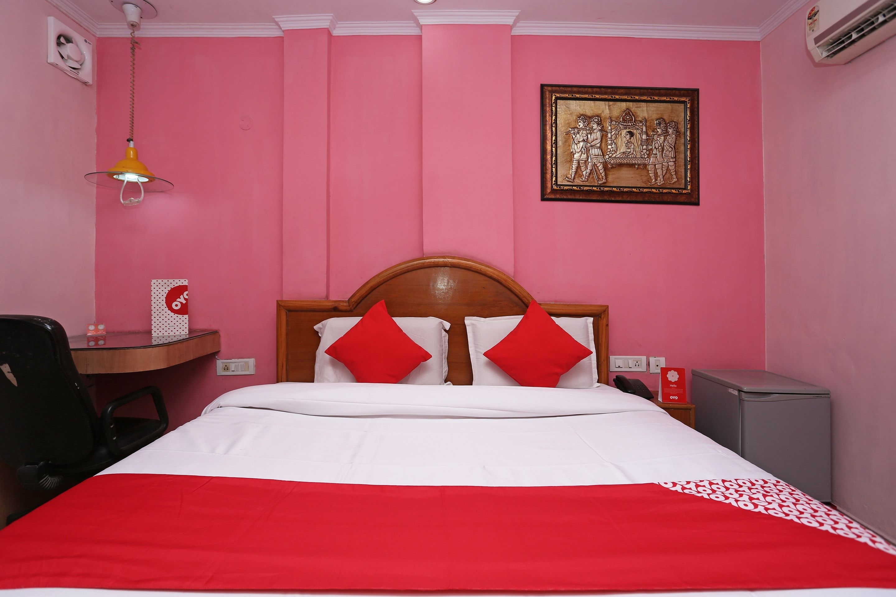 A hotel room with a bed, a desk, a chair, a telephone, and an air conditioning unit.