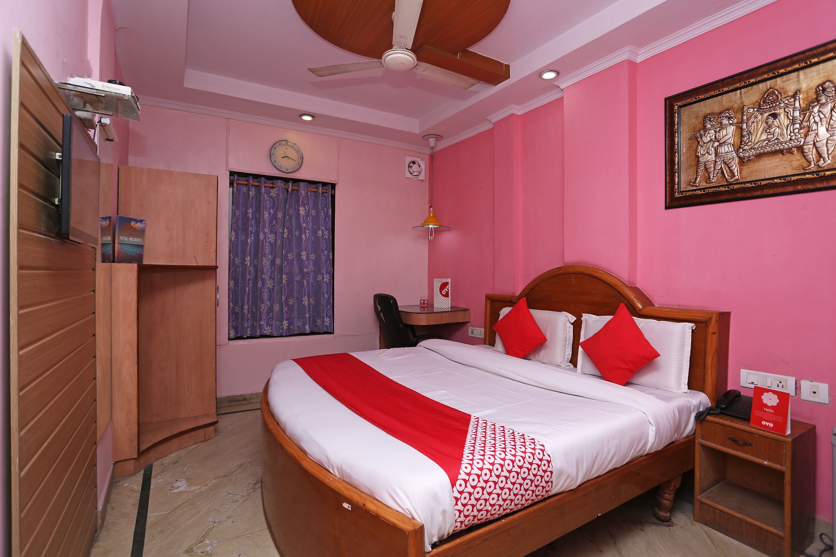 Een hotelkamer met een bed, een bureau, een stoel, een kledingkast, een klok en een schilderij aan de muur.