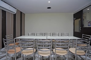 A conference room with a rectangular table surrounded by metal chairs with wooden seats, a white ceiling with recessed lighting, and a wall-mounted air conditioning unit. - Super Hotel O by OYO Raj Palace (Meerut)