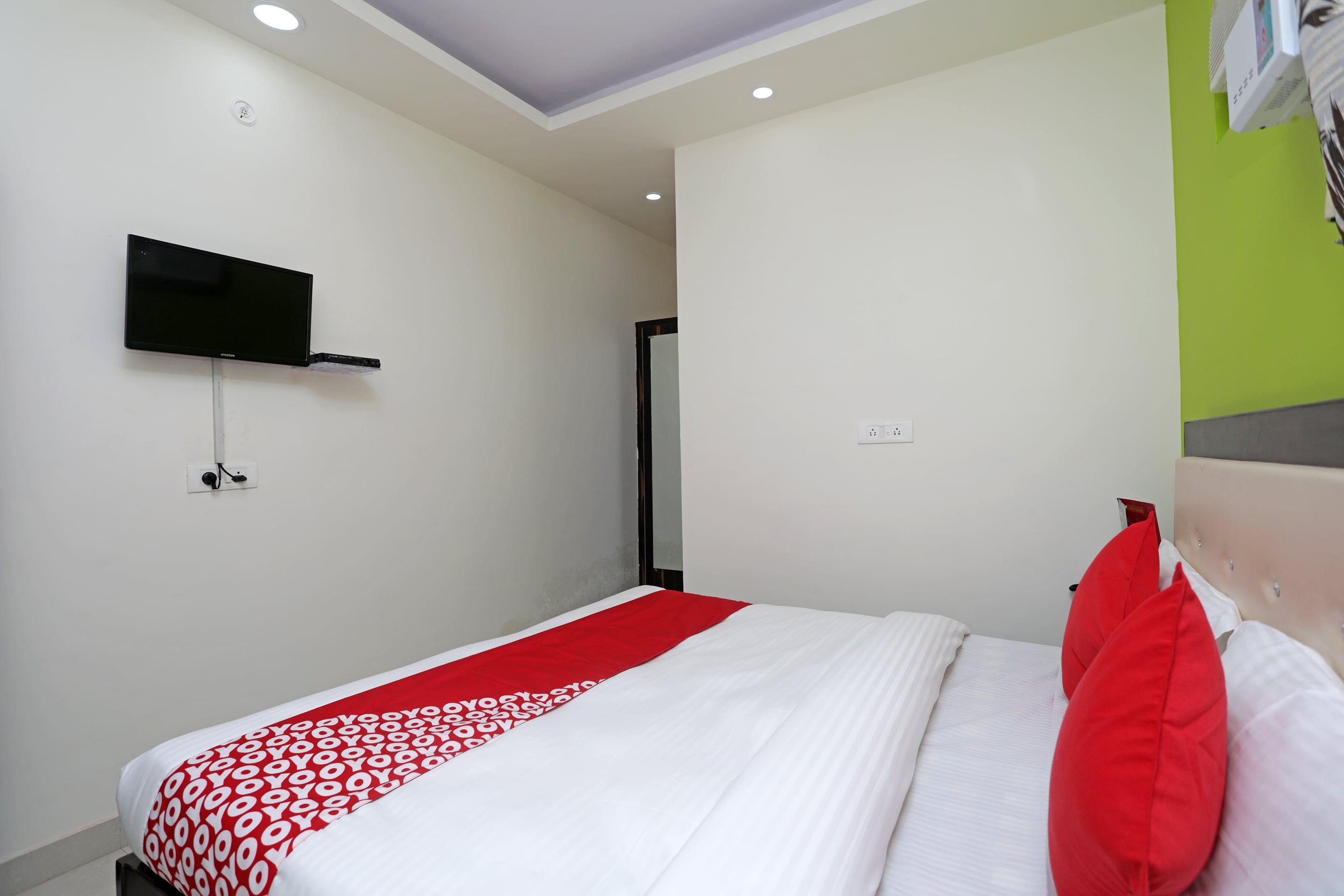 Une chambre d’hôtel avec un lit, un téléviseur fixé au mur et un mur d’accent de couleur verte.