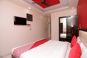 Habitación de hotel con cama, televisión de pantalla plana, ventilador de techo y puerta que da a otra habitación.