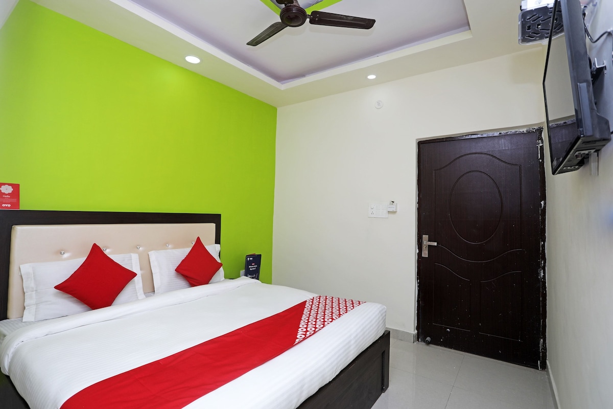 A hotel room with a bed, a ceiling fan, a TV mounted on the wall, and a door.