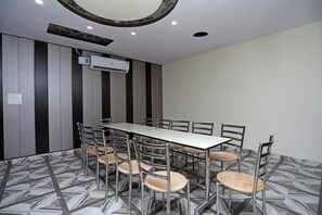 Un salón de conferencias con una mesa rectangular rodeada de sillas, una unidad de aire acondicionado en la pared y un suelo con diseño.