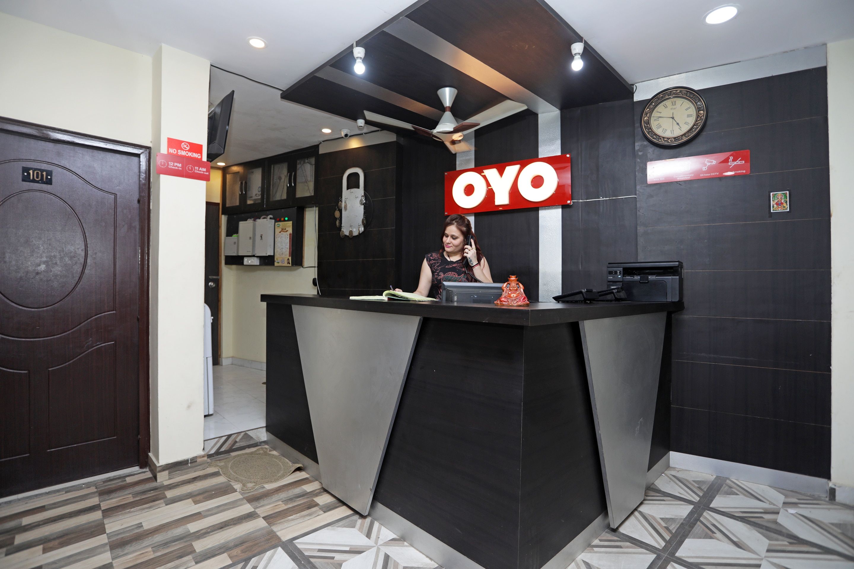 A reception desk with a 'OYO' sign, a clock, and a 'NO SMOKING' sign.