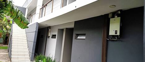 Um edifício moderno com telhado plano, várias varandas e uma pequena área de jardim com grama e plantas.