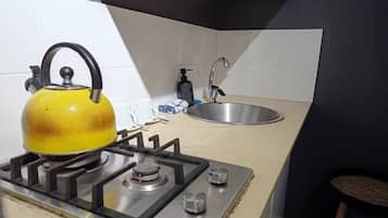 A kitchen with a gas stove, a kettle, a sink, and a bar stool.
