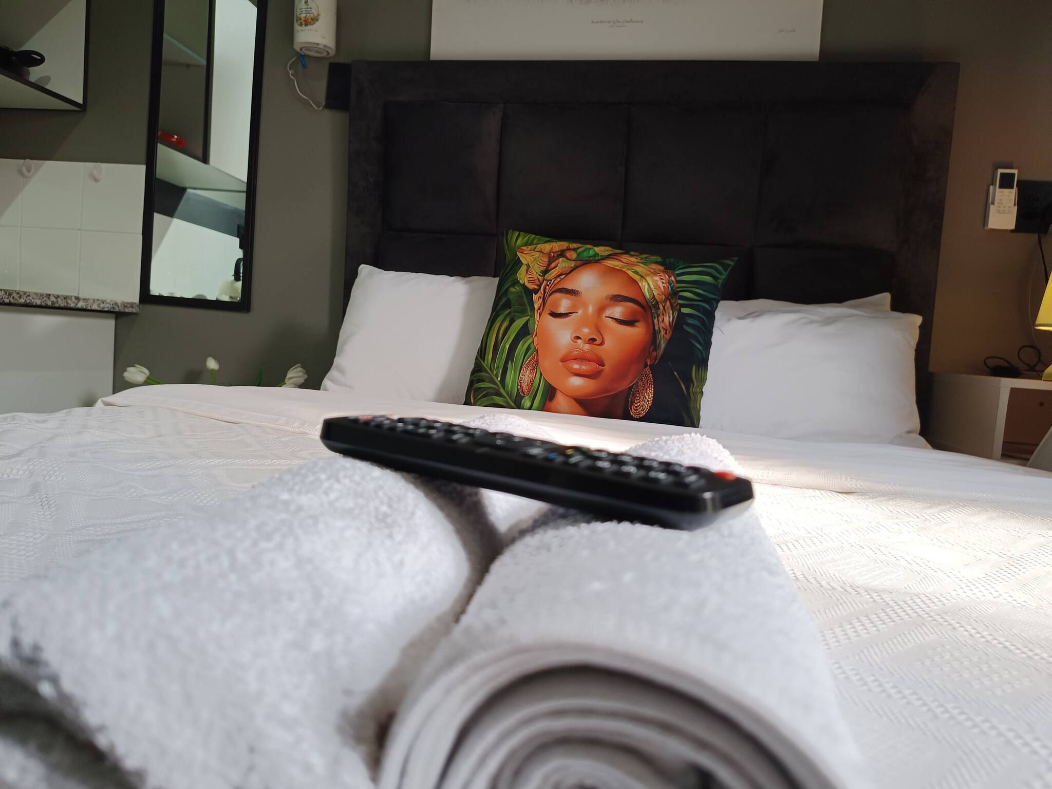A hotel room with a bed, a remote control, and a rolled-up magazine on the bed.