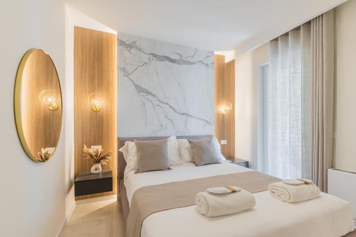 A modern hotel room with a large bed, a marble wall, and a large window with curtains.