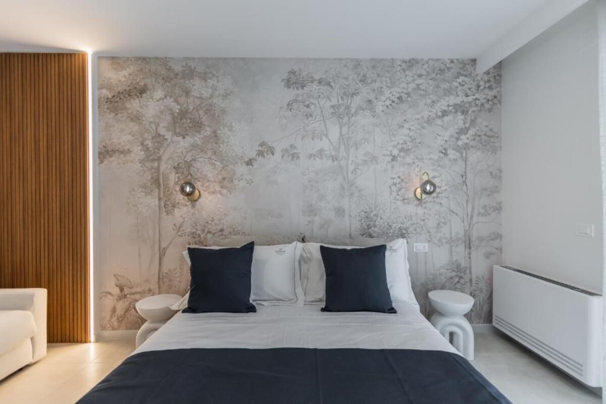 A modern bedroom with a large bed, two bedside tables, a white radiator, and a wall with a tree pattern.