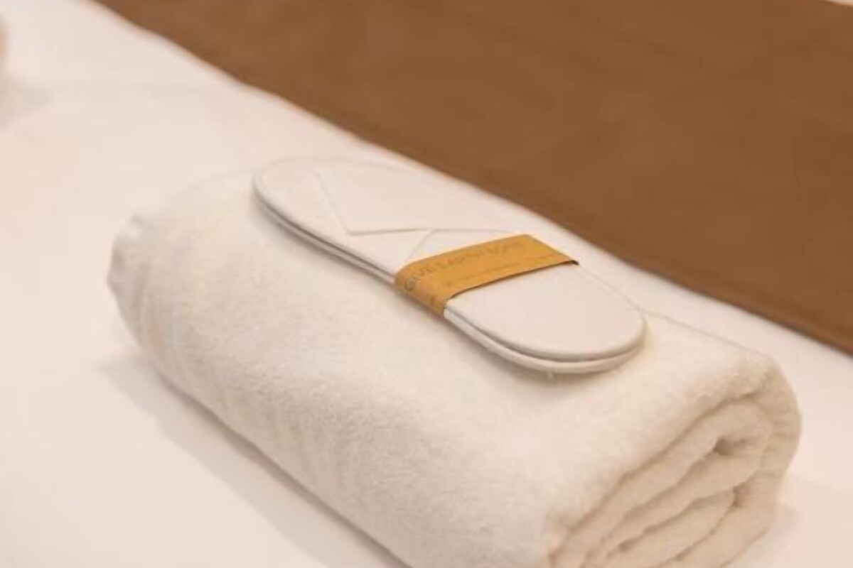 A neatly folded white towel with a brown tag on a bed with a brown bedspread.